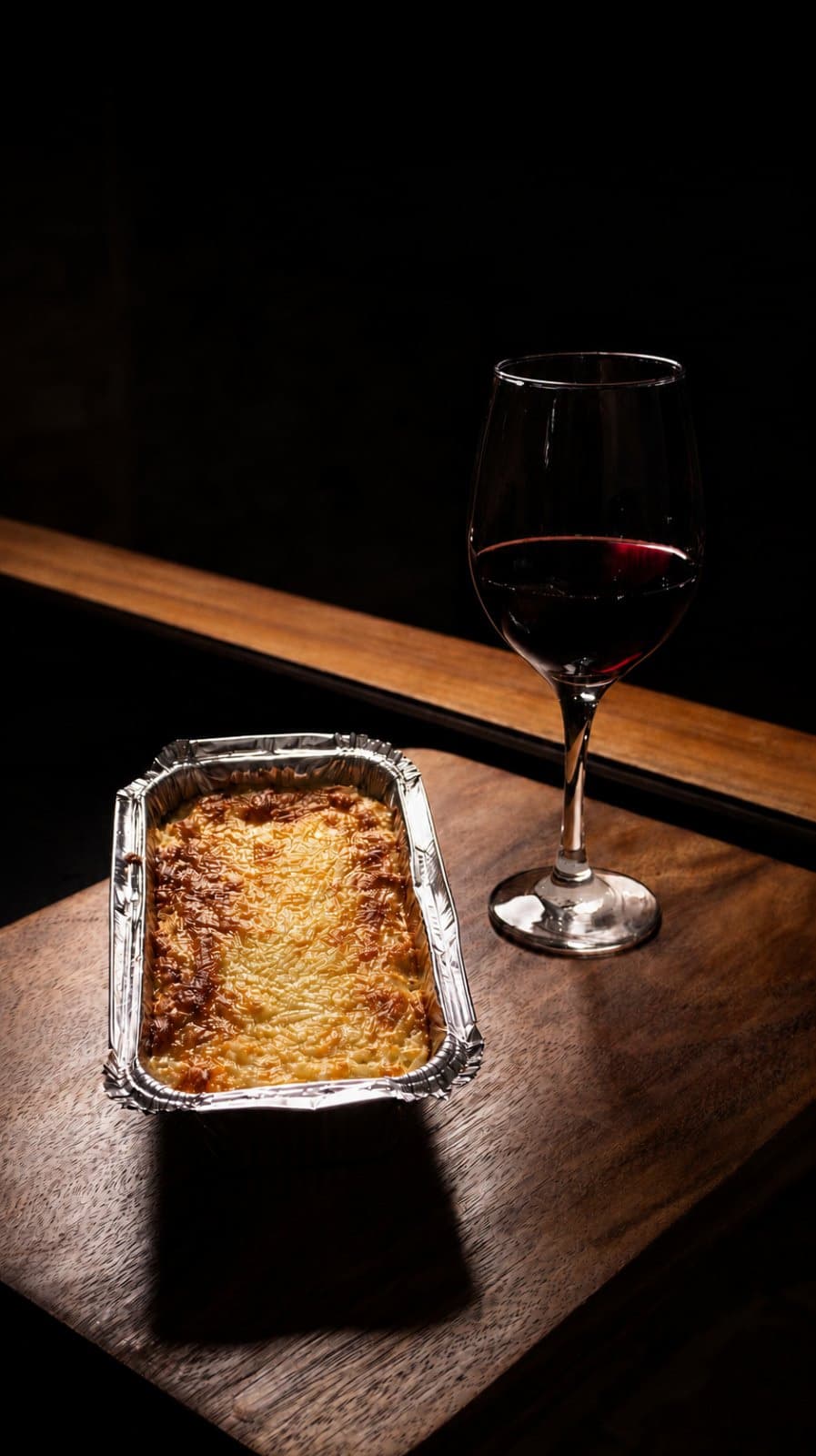 Pasta al horno junto a una copa de vino, con corrección de color aplicada.