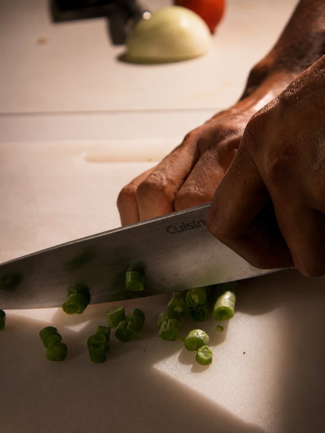 Manos cortando cebollín sobre una tabla, en plena preparación de cocina.